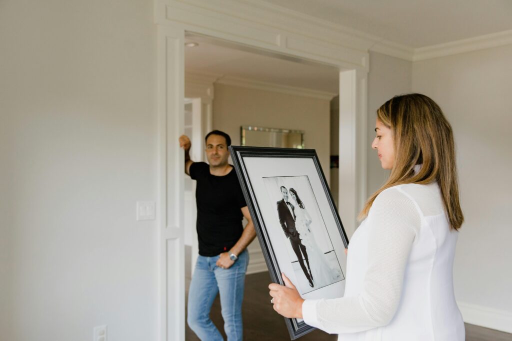 A couple stands in a modern room, admiring a framed wedding photograph, symbolizing love and togetherness.